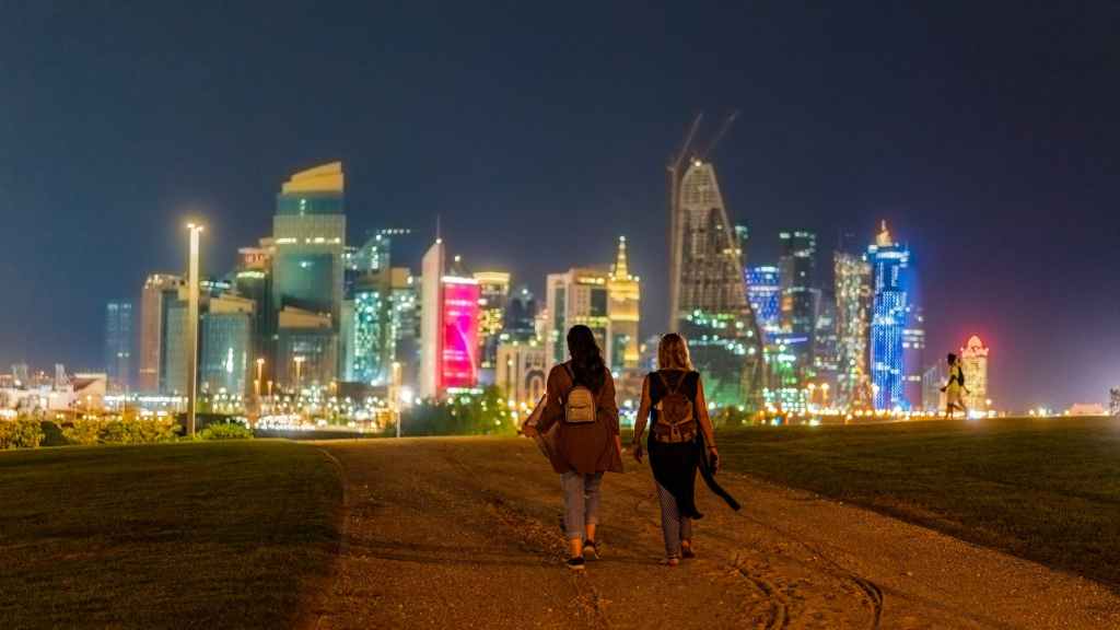 anonymous women walking in city near illuminated skyscrapers at night