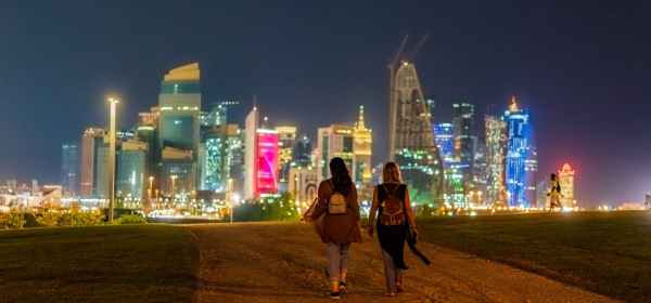 anonymous women walking in city near illuminated skyscrapers at night